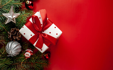 Christmas composition on a red background with a white gift box, with a red ribbon with fir branches, toys, copy space for your congratulations