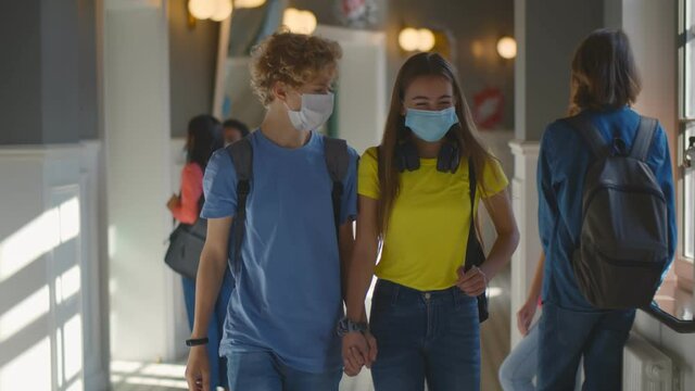 High school boy and girl students in mask walking in corridor holding hands