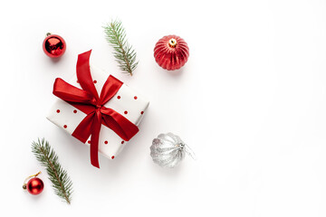 Christmas composition on a white background with a white gift box, with a red ribbon with fir branches, toys, copy space for your congratulations