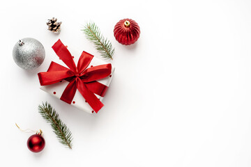 Christmas composition on a white background with a white gift box, with a red ribbon with fir branches, toys, copy space for your congratulations