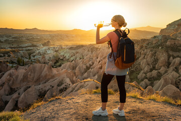 Woman backpacker drinking water at top of the mountain with breathtaking view on the valley during...