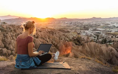 Tuinposter Young girl working at laptop at sunset on top of mountain with beautiful view at valley © 22Imagesstudio