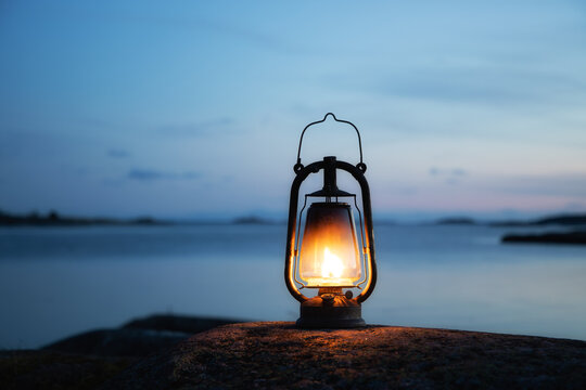 Large oil lamp outdoors in the dark. Old lantern illuminates on the sea shore. Rocks and sunset sky.