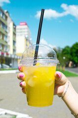 In a female hand, a cocktail drink with a yellow straw. The background is blurred.