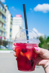 In a female hand, a cocktail drink with a red straw. The background is blurred.