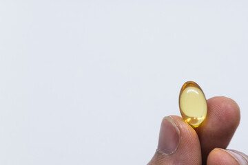 On a white background, they hold in their fingers one yellow capsule. Vitamins