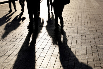 Silhouettes and shadows of people on the city street. Crowd walking down on sidewalk, concept of...