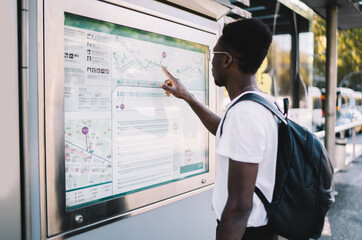Young african american male looking at city public transport map choosing route for transportation,...