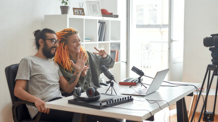 Hi guys. Female and male blogger saying hello, greeting subscribers while recording video blog or...