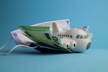 kleines Flugzeug mit Schutzmaske und Geld steht für Stornierungskosten bei Flugreisen 