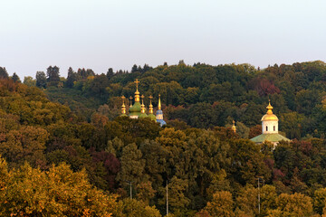 Naklejka premium Picturesque morning autumn landscape view of famous Kyiv's hills against blue sky. The domes Saint George's Cathedral and ancient Michael's Cathedral of Vydubychi Monastery over the old trees. Kyiv