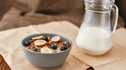 Close up of homemade granola in a plate with nuts, honey, blueberries and banana served on napkin, Fresh milk in glass jug