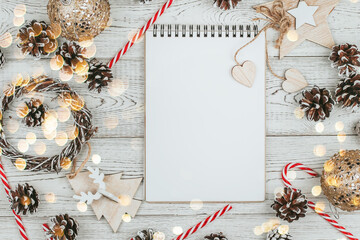Blank notepad page surrounded by pine cones and New Year's decor on a white wooden background copy space. Christmas wishlist