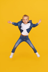 Full length portrait of excited little child boy Jumping for joy isolated on yellow background.
