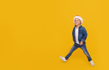 Fototapeta na wymiar Portrait of a satisfied little child boy dressed in christmas Santa hat. laughing isolated over colored yellow background. Wow face. full-length portrait