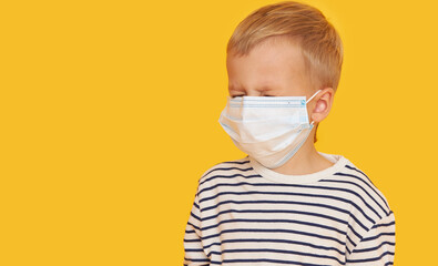 Portrait of sick little child boy wearing protective mask on yellow background. Virus protection and healthcare concept during COVID pandemic