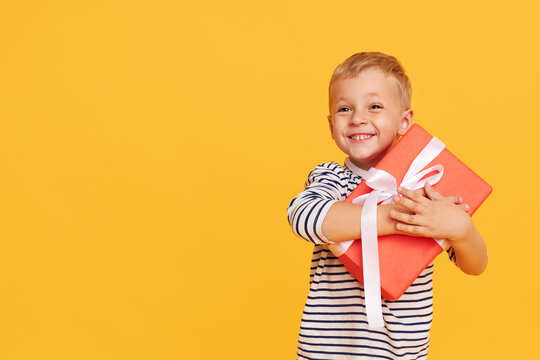 Studio shot of happy child boy celebrating holiday, unpacking gift box with excited face, posing over yellow background