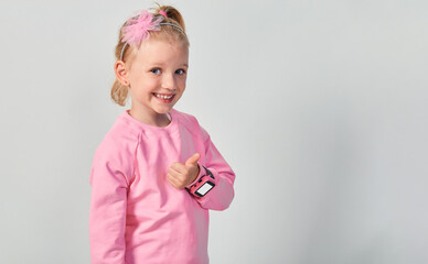 Cute caucasian little girl 4-5 year old wearing a smart watch on her wrist. Technology for children, against gray studio background