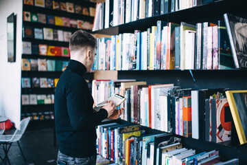 Unrecognizable student with clipboard searching for book in library