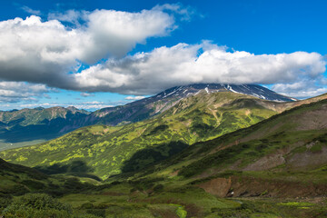 Panoramic view of the mountain valley with cloud shadows on the slopes. The top of the volcano is covered by a cloud
