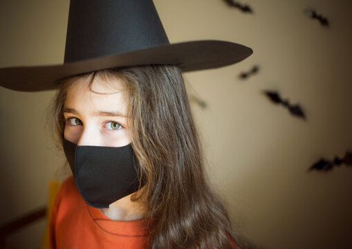Halloween and coronovirus. portrait of child in reusable black protective mask and witch hat on background of bats