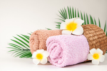 Obraz na płótnie Canvas Pastel towels with Plumeria flowers with tropical palm leaves on light background with copy space. Skin care and spa concept.