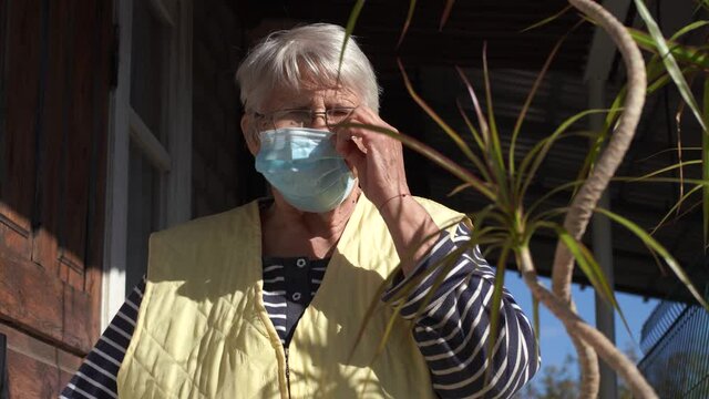 Older woman wear the protective face mask. Old lady put on a mask next to the door. Outdoors 4K footage. Stay at home and wear a mask during the covid-19