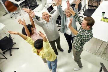 Group of diverse employees raising hands in the air, hoping for success on their plans while standing in the office, Aged woman and man, senior interns having first day at work