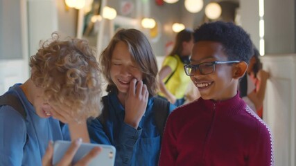 Diverse schoolboys watching funny video on smartphone in school corridor