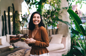 Delighted ethnic woman messaging via smartphone on veranda