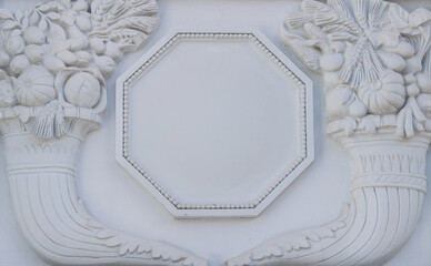 A white floral plaster relief on a white plastered wall.