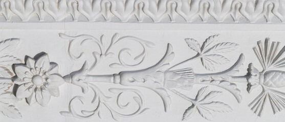 A white floral plaster relief on a white plastered wall.