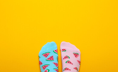 Female feet in pink and blue socks in watermelon print on a pastel yellow background. Top view.Copy space.