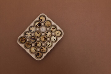 Quail eggs in package on brown background with copy space. Top view