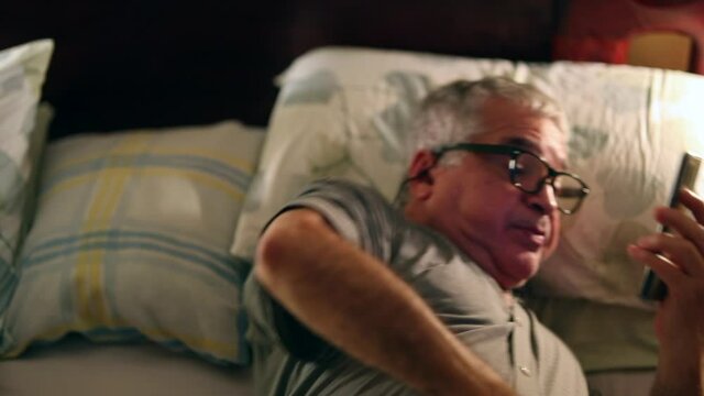 Older man watching cellphone screen at night in bed