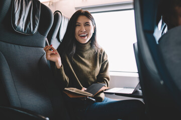 Laughing woman looking at camera and making notes in diary in train