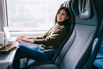 Cheerful ethnic woman using laptop in bus