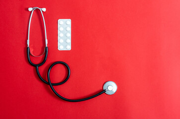 Flat lay of stethoscope and pills on red background