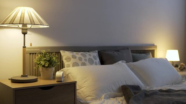 cozy modern illuminated bedroom with a bedside lamp and white double bed covered by grey sheet cover in an apartment.