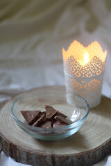 Bowl of chocolate, lit candle and wooden tray on a bed. 