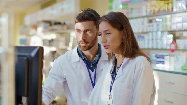 Two medical workers man and woman cooperating in apothecary. Professional adult pharmacist coaching female intern. Collaboration. Medication, healthcare, drugs.