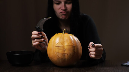 Young brunette woman carves a pumpkin for Halloween. Preparation for the holiday.