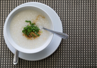 Boiled rice in a white bowl with vegetables sprinkled on top with a spoon, placed on a gray background, Top view.