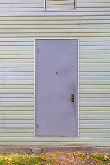 Part of the wall of a white board building with a closed door