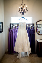 white wedding dress hanging on wall or window with bridesmaids dresses in background