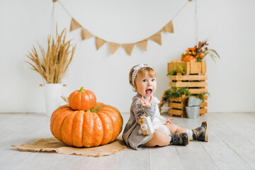 Little girl plays with a big pumpkin. Children's photo zone in autumn style.