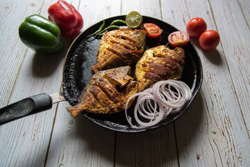 Close up of tandoori pomfret fish in a black pan along with ingredients on a background - obrazy, fototapety, plakaty
