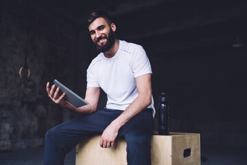 Cheerful caucasian male trainer in active wear using digital tablet for blogging and share content...