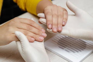 Female hardware manicure in the salon. The technician holds the hands of the client and examines the nails before processing.