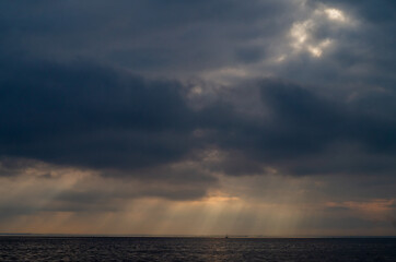 Naklejka na ściany i meble sun rays shine through the clouds at sunrise, sea background.